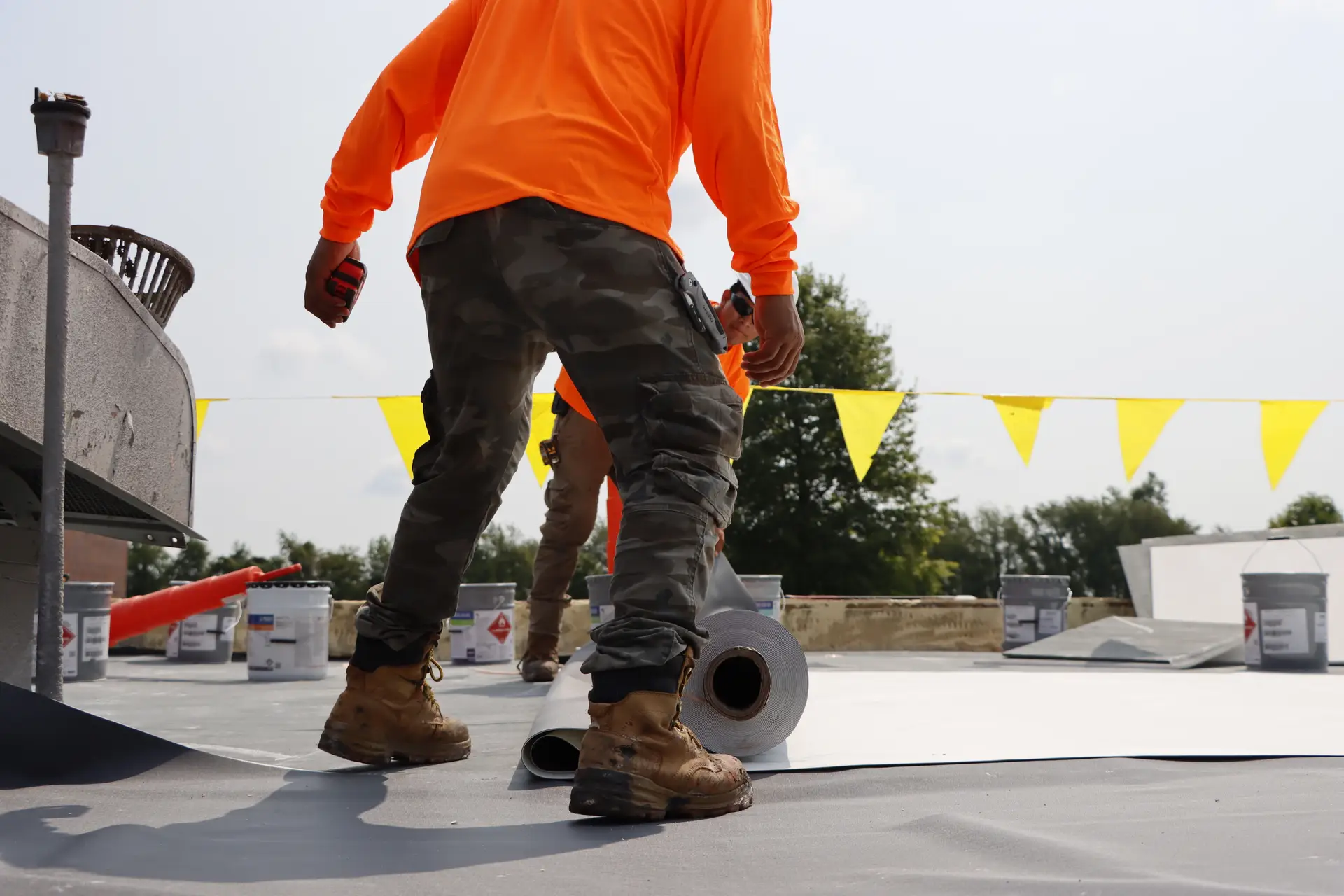 Commercial roofing service crew unrolling TPO membrane material on a flat roof installation site